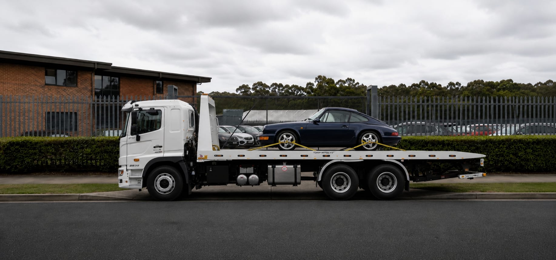 A tilt tray arriving at a storage yard gate with a car on the deck